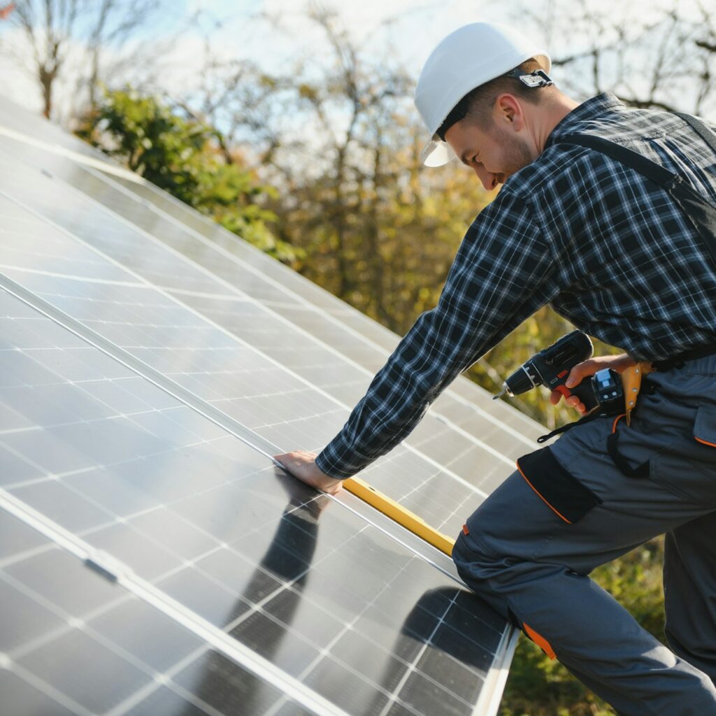 Male worker in uniform outdoors with solar batteries at sunny day.